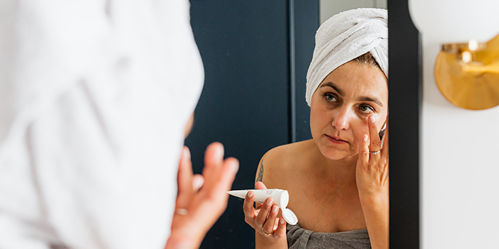 woman putting on moisturizer looking into mirror