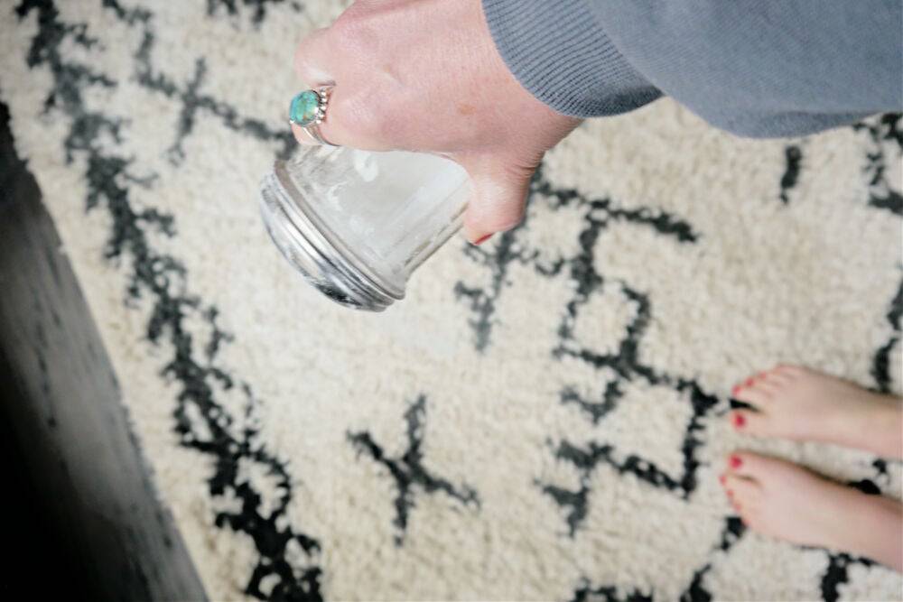 Espolvorea bicarbonato de sodio sobre la alfombra con la mano.